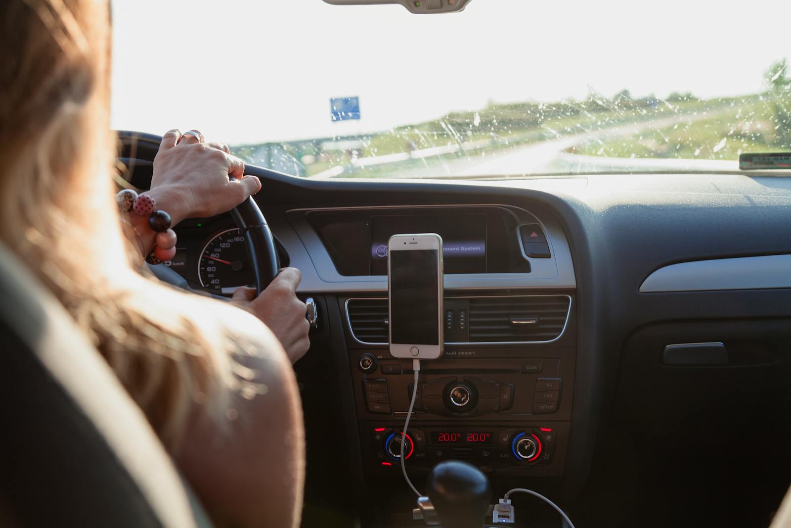 auto View from behind a woman driving a car on a sunny day with a phone mounted on the dashboard.